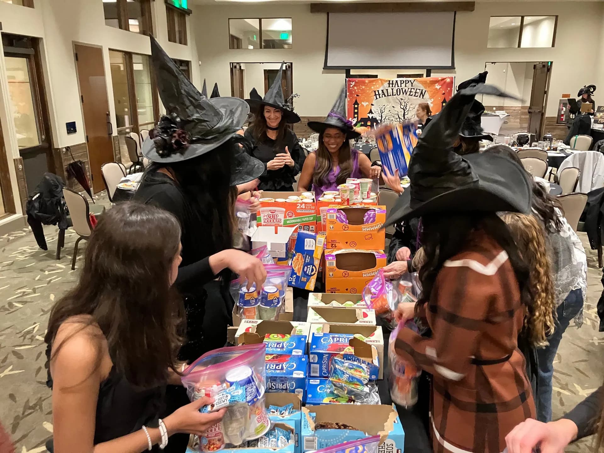 Witches sorting boxes of food into Weekend Meal Kits